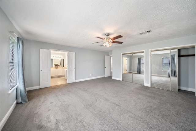 unfurnished bedroom featuring carpet, baseboards, visible vents, multiple closets, and a textured ceiling