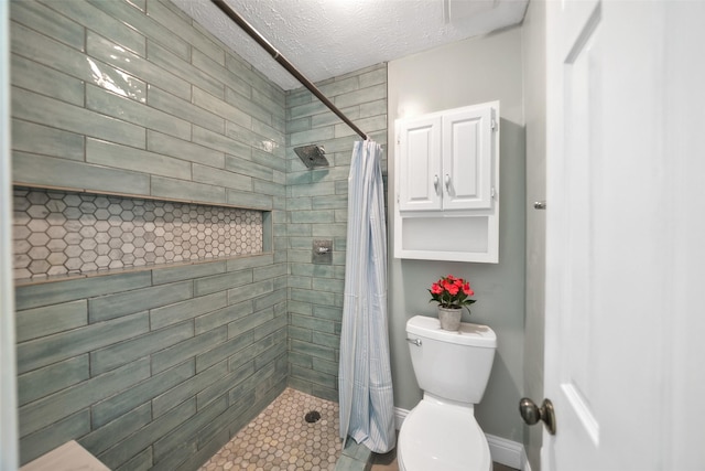 full bathroom with a tile shower, a textured ceiling, toilet, and baseboards