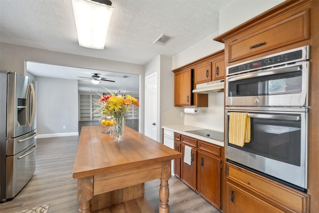 kitchen with under cabinet range hood, visible vents, light wood finished floors, and appliances with stainless steel finishes