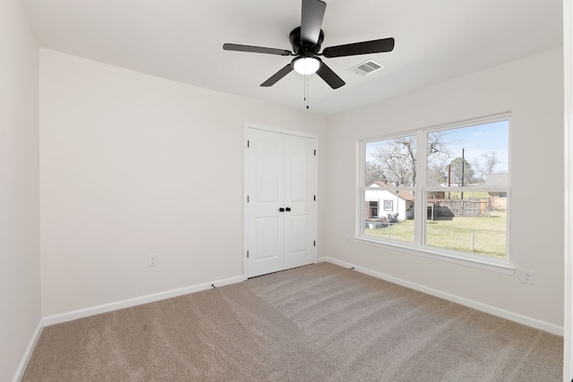 unfurnished room with visible vents, carpet floors, baseboards, and a ceiling fan