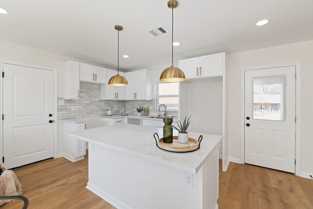 kitchen with visible vents, light wood-style flooring, a sink, hanging light fixtures, and white cabinets