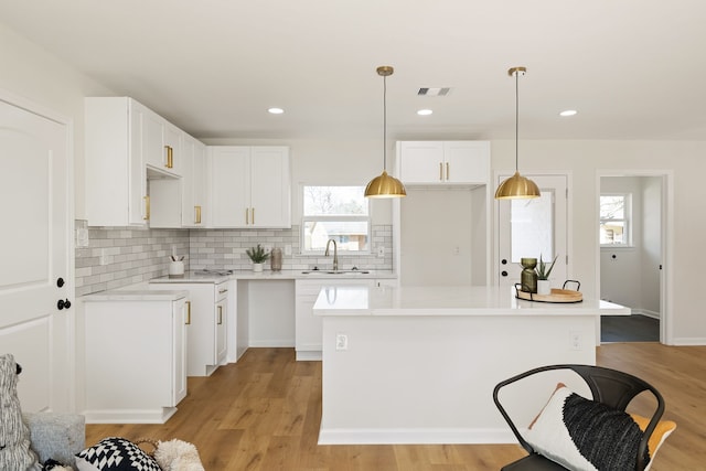 kitchen featuring visible vents, backsplash, light wood-style flooring, white cabinets, and a sink