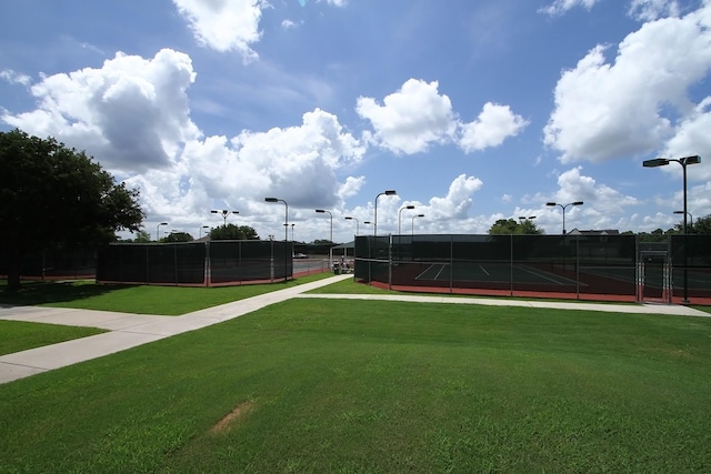 view of community with a tennis court, a lawn, and fence