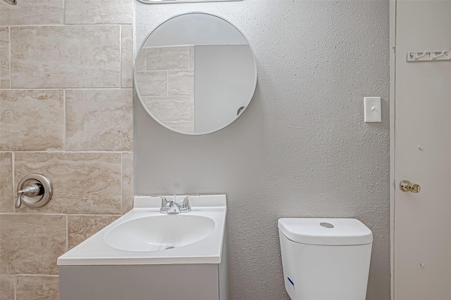 bathroom with vanity, toilet, and a textured wall