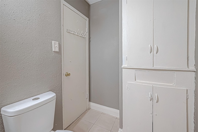 bathroom with tile patterned flooring, toilet, a textured wall, and baseboards