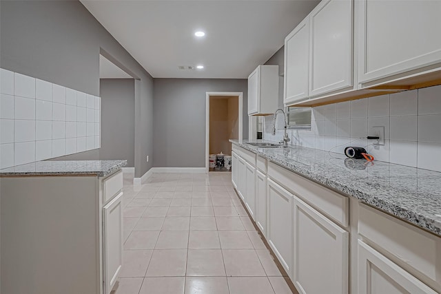 kitchen featuring a sink, decorative backsplash, light stone countertops, and light tile patterned flooring