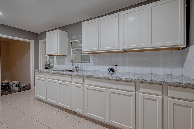 kitchen with tasteful backsplash, white cabinetry, light stone counters, and a sink