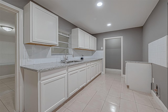 kitchen with a sink, tasteful backsplash, white cabinets, light tile patterned floors, and light stone countertops