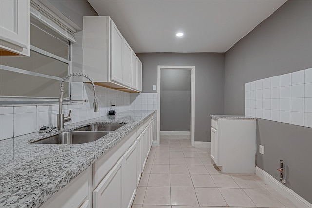 kitchen featuring tasteful backsplash, baseboards, light stone counters, white cabinetry, and a sink