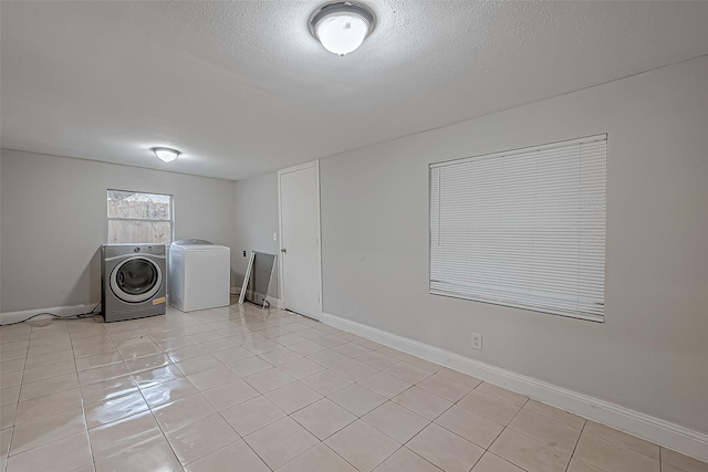 laundry room featuring a textured ceiling, light tile patterned floors, baseboards, and washing machine and clothes dryer