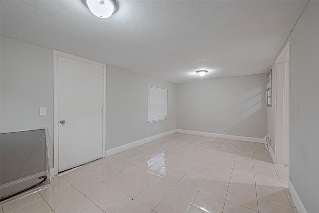 below grade area with light tile patterned floors, baseboards, and a textured ceiling