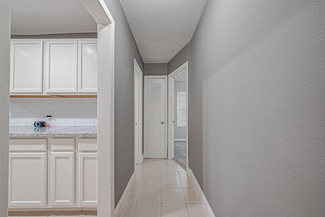 corridor featuring light tile patterned flooring, a textured ceiling, baseboards, and a textured wall