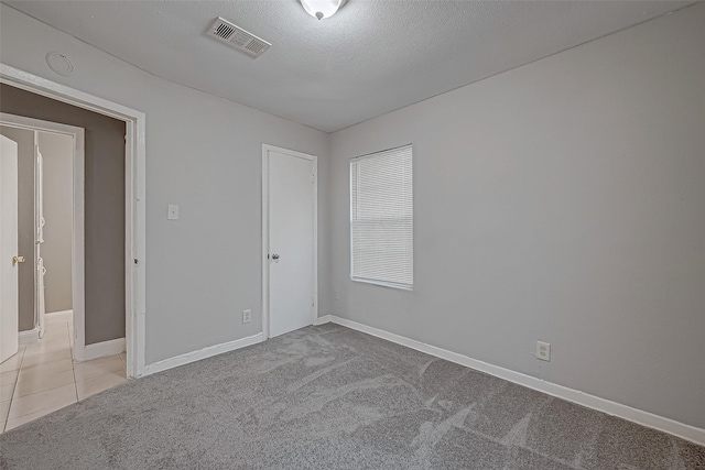 carpeted spare room with tile patterned floors, baseboards, visible vents, and a textured ceiling