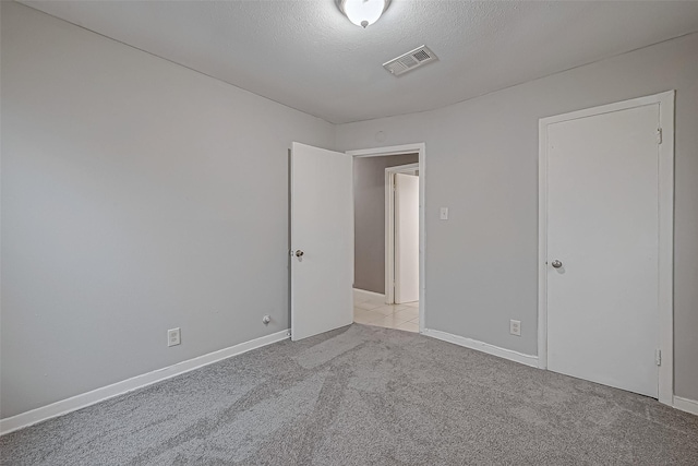 unfurnished room with a textured ceiling, baseboards, visible vents, and light carpet