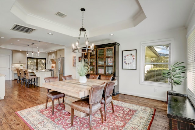 dining space with a tray ceiling, light wood-style flooring, and visible vents