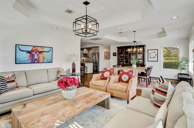 living room featuring visible vents, crown molding, a chandelier, light wood-style flooring, and a raised ceiling