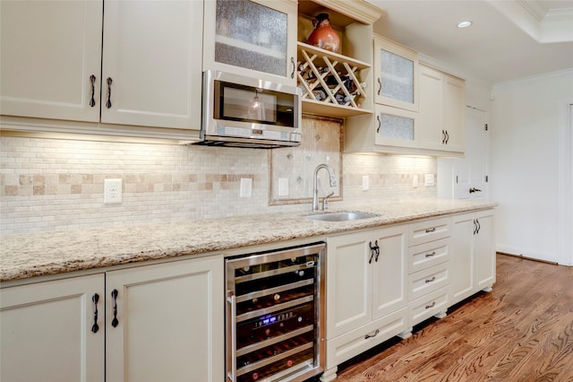 kitchen with beverage cooler, light wood-style flooring, a sink, crown molding, and stainless steel microwave