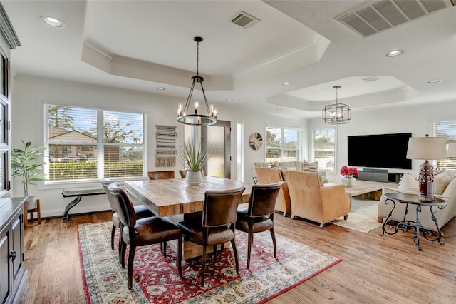 dining space with a tray ceiling, visible vents, light wood-style flooring, and ornamental molding