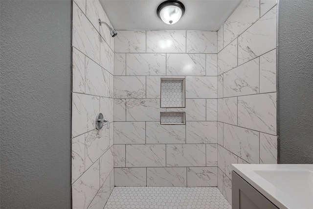 bathroom featuring vanity, a textured wall, and a tile shower