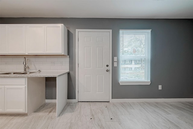 interior space featuring white cabinetry, baseboards, backsplash, and a sink