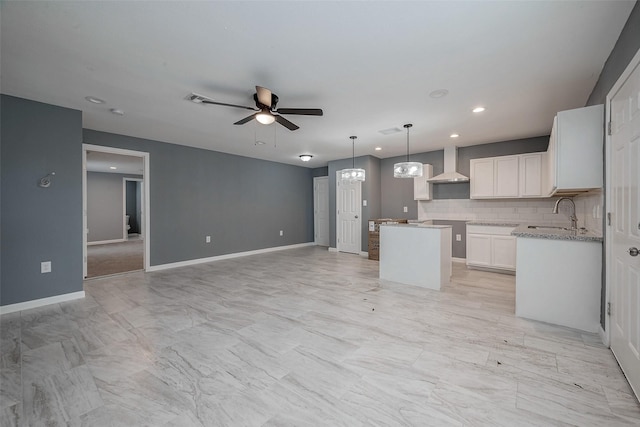 kitchen with a kitchen island, a sink, decorative backsplash, wall chimney exhaust hood, and ceiling fan with notable chandelier