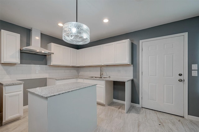 kitchen with light stone countertops, a sink, white cabinets, wall chimney range hood, and backsplash