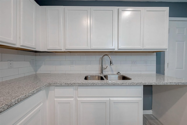 kitchen featuring light stone counters, decorative backsplash, white cabinets, and a sink