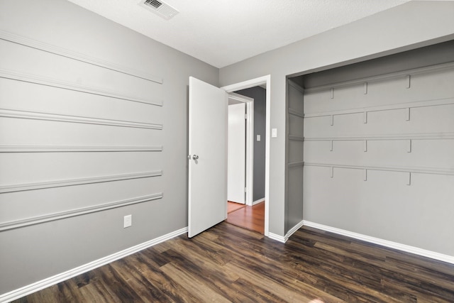 unfurnished bedroom featuring dark wood-style floors, visible vents, a closet, and baseboards