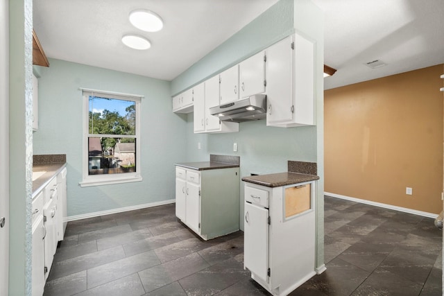 kitchen with under cabinet range hood, baseboards, dark countertops, and white cabinetry