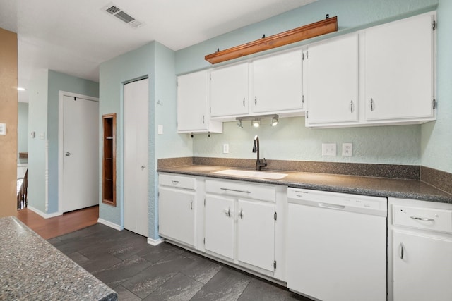 kitchen with dark countertops, visible vents, white dishwasher, white cabinets, and a sink