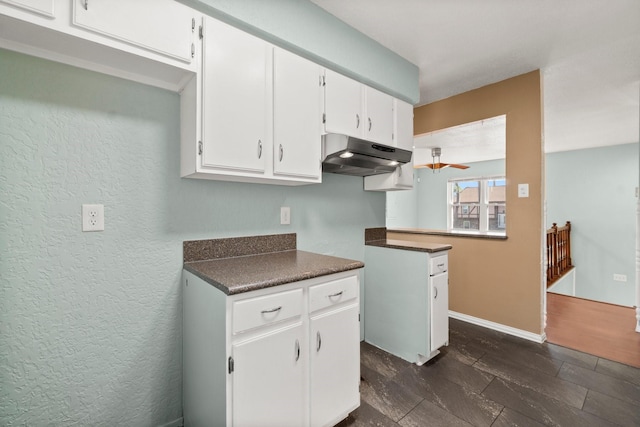 kitchen featuring under cabinet range hood, baseboards, dark countertops, and white cabinetry