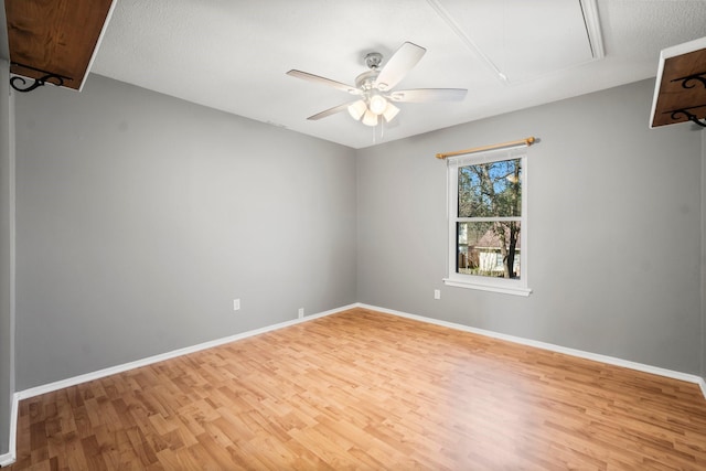 empty room with attic access, light wood-style flooring, a ceiling fan, and baseboards