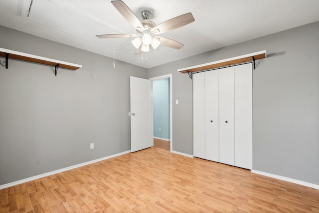 unfurnished bedroom featuring baseboards, attic access, ceiling fan, light wood-style floors, and a closet