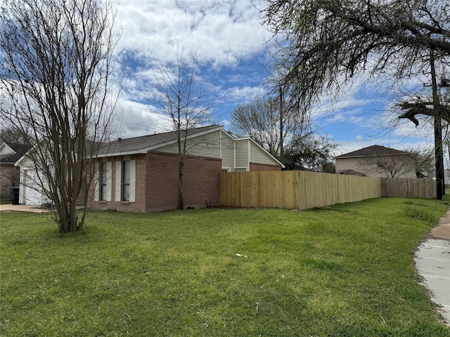 view of side of home featuring a garage, brick siding, a lawn, and fence