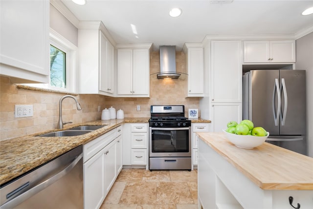 kitchen with butcher block countertops, a sink, white cabinetry, stainless steel appliances, and wall chimney exhaust hood