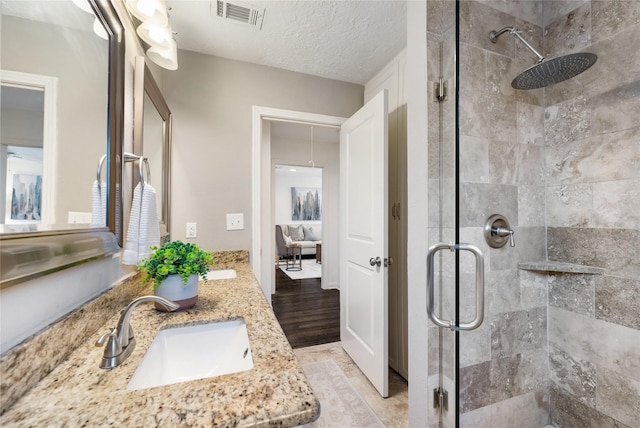 ensuite bathroom with visible vents, a shower stall, double vanity, a textured ceiling, and a sink