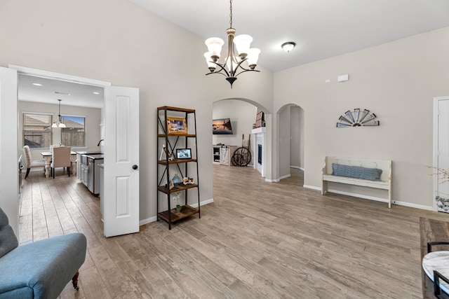 sitting room featuring arched walkways, a notable chandelier, light wood finished floors, and baseboards