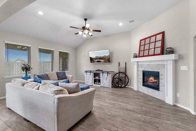 living room featuring visible vents, lofted ceiling, wood finished floors, baseboards, and a brick fireplace