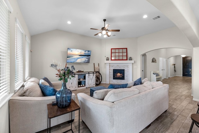 living area featuring visible vents, wood finished floors, arched walkways, lofted ceiling, and a brick fireplace