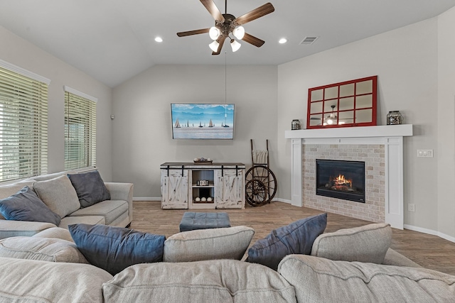 living room featuring visible vents, wood finished floors, baseboards, a brick fireplace, and vaulted ceiling