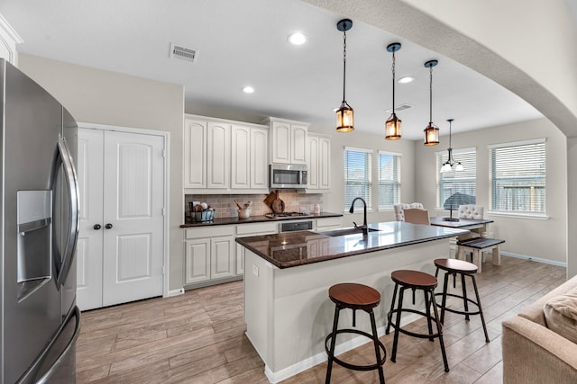 kitchen featuring visible vents, a breakfast bar, a sink, stainless steel appliances, and backsplash