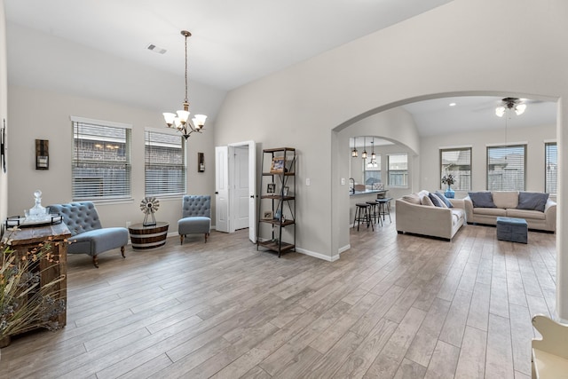 living area with visible vents, wood finished floors, arched walkways, an inviting chandelier, and vaulted ceiling