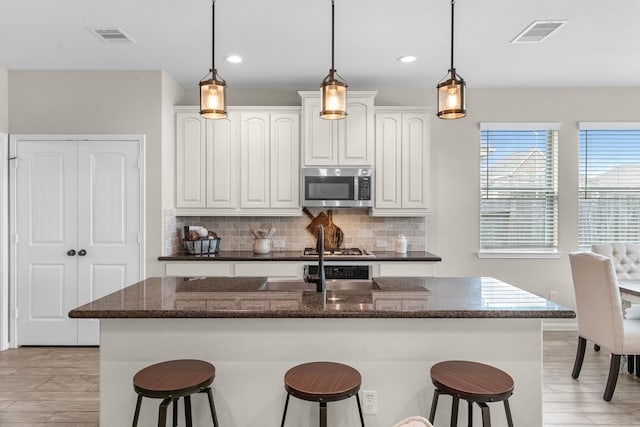 kitchen with tasteful backsplash, stainless steel microwave, a kitchen breakfast bar, and visible vents