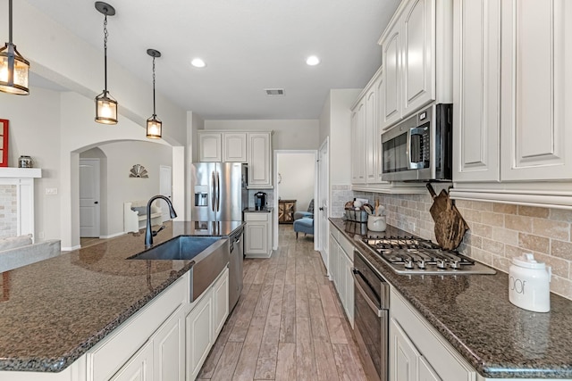 kitchen featuring tasteful backsplash, light wood-style floors, arched walkways, stainless steel appliances, and a sink