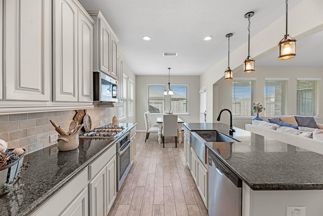 kitchen with a sink, backsplash, light wood-type flooring, stainless steel appliances, and a kitchen island with sink