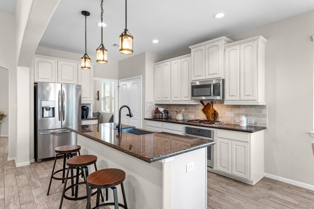 kitchen featuring dark stone countertops, light wood-style flooring, a sink, appliances with stainless steel finishes, and backsplash