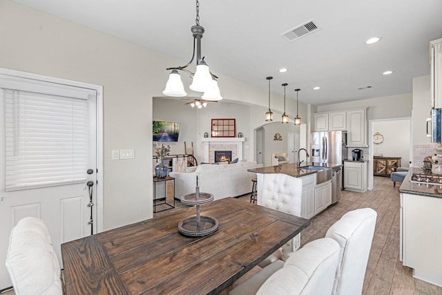 dining space featuring visible vents, recessed lighting, light wood-style floors, a lit fireplace, and ceiling fan