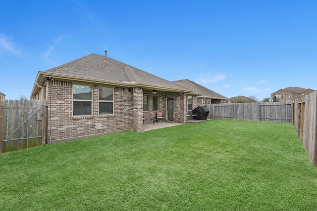 back of house with a fenced backyard, a shingled roof, a lawn, a patio area, and brick siding