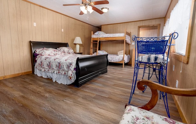 bedroom featuring ornamental molding, wood finished floors, wooden walls, baseboards, and ceiling fan