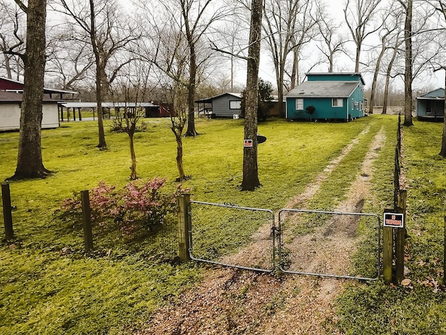 view of yard featuring fence, an outdoor structure, driveway, and a gate